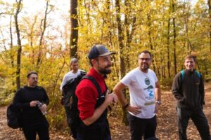four men standing in a forest one has a backpack they are happy and on a hike